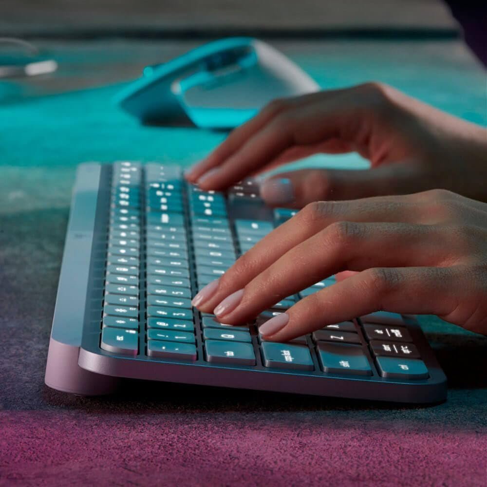 Close-up of hands typing on an illuminated computer keyboard, with a wireless mouse in the background on a desk.