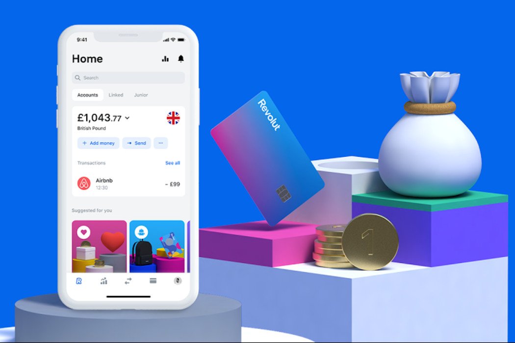 A smartphone displaying a Revolut banking app, a Revolut card, coins, and a money bag on geometric shapes against a blue background.