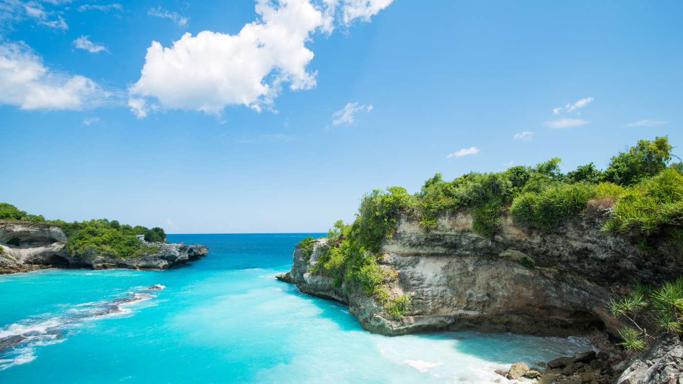 Clear turquoise water flows between rocky cliffs under a bright blue sky with scattered clouds. Lush green vegetation covers the cliff tops. Clear turquoise water flows between rocky cliffs under a bright blue sky with scattered clouds. Lush green vegetation covers the cliff tops.