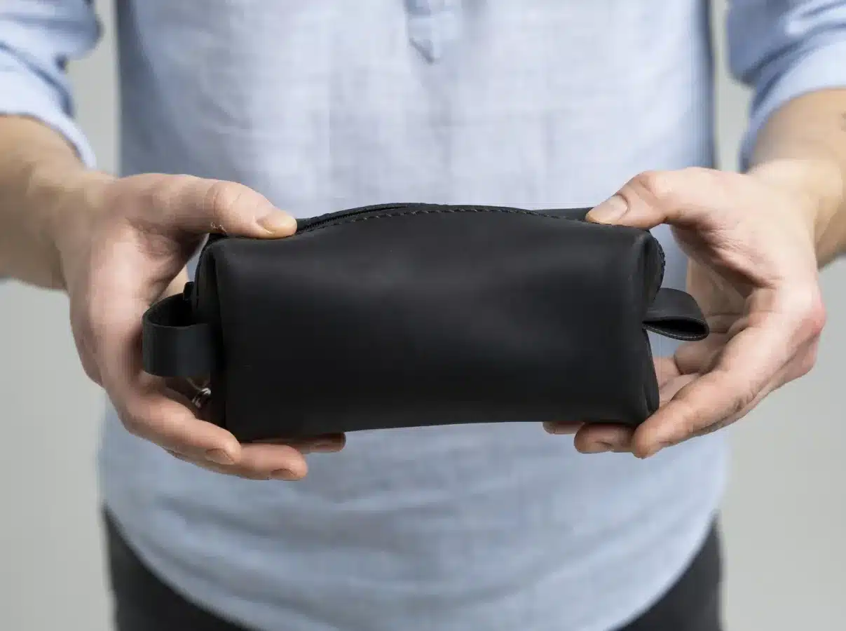A man holding a black leather toiletry bag.