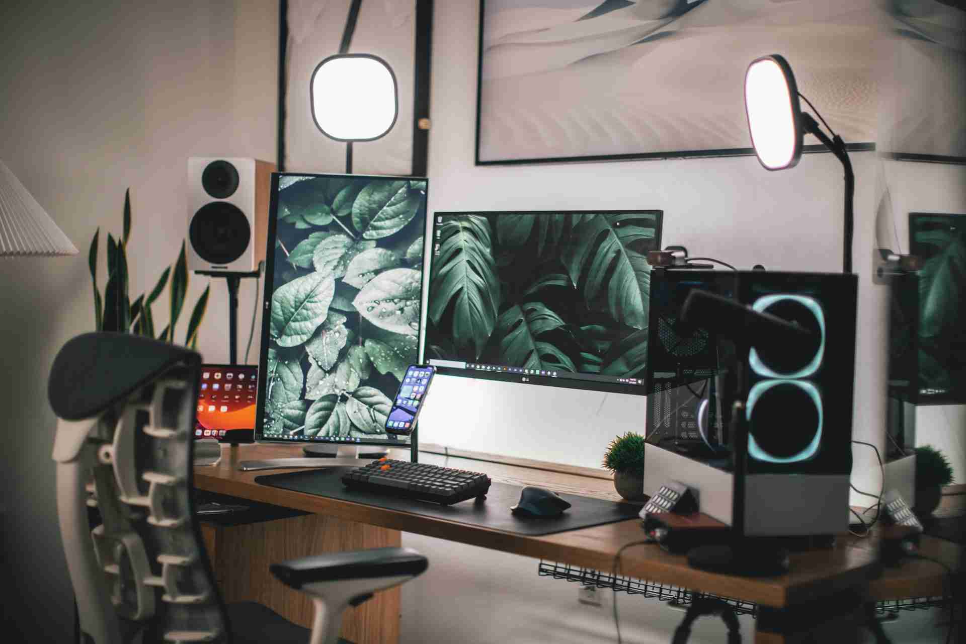 A desk with two monitors and a lamp on it.